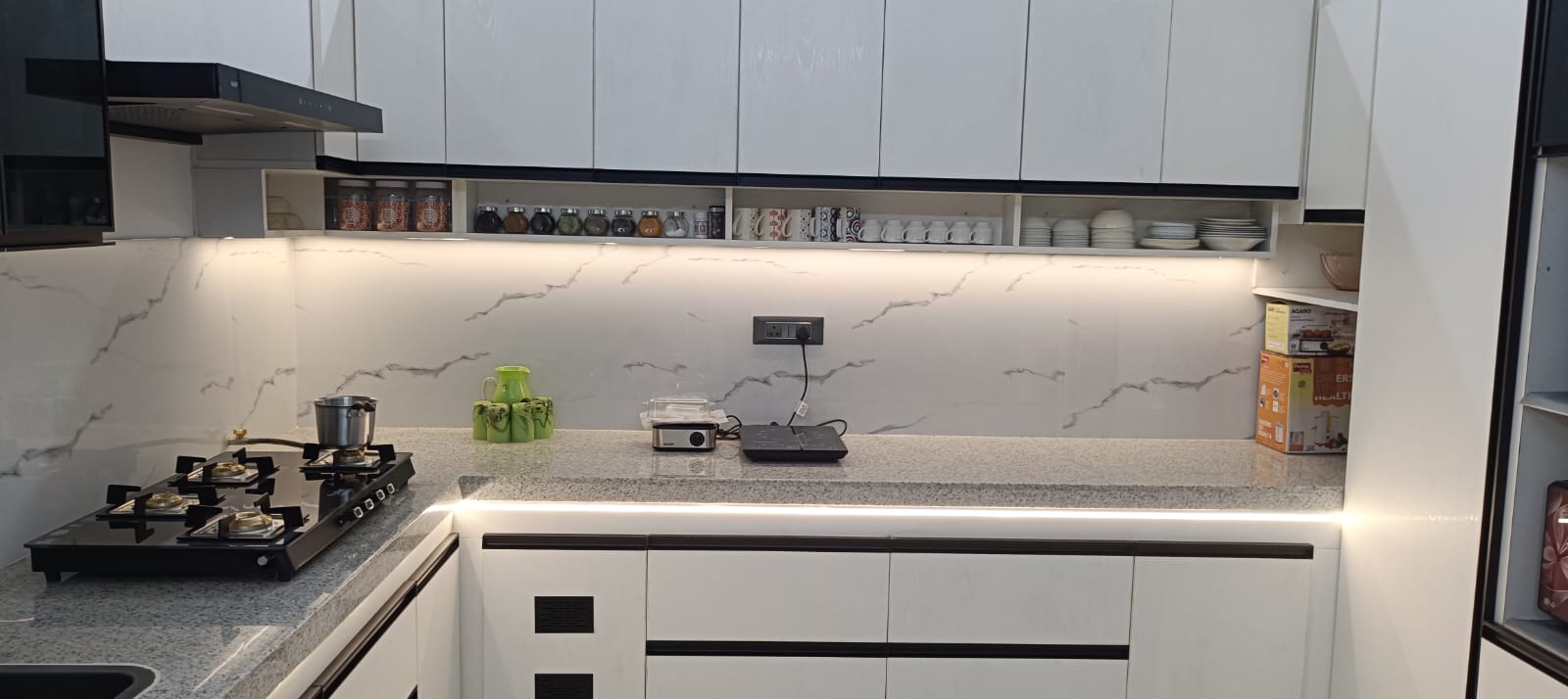 Completed modern kitchen with white cabinetry, stone worktops, open shelving, and task lighting