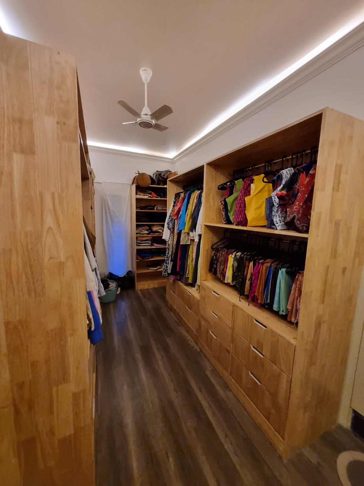 Walk-in wardrobe with open timber hanging spaces, shelving, and fitted drawers