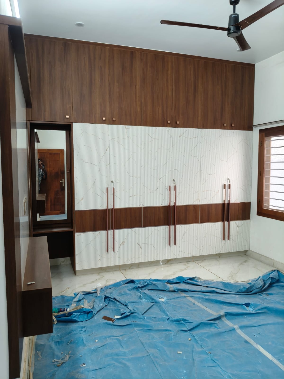 Bedroom wardrobe with light patterned fronts, long handles, overhead storage, and dressing mirror